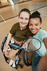 Vertical high angle portrait of young woman in wheelchair taking selfie with friend at indoor...