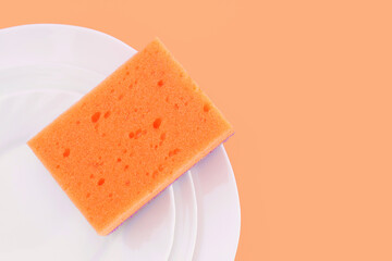 Orange sponge on white plates on yellow background. Dishwashing and household cleaning tools. Tool for having dish and kitchenware clean.