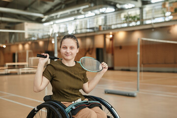 Portrait of active young woman in wheelchair looking at camera in indoor sports court