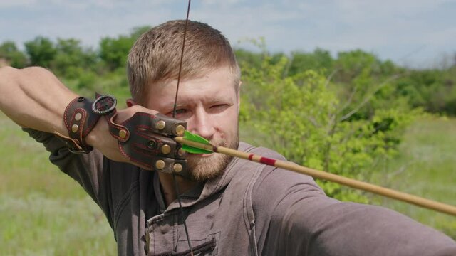 a young guy shoots a bow at a target, in nature, and hits the target, the arrow pierces the target for flight, pulls the bowstring tightly for a shot. Prores 422