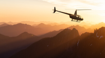 Black Helicopter flying over the Canadian Rocky Mountains. Dramatic Sunrise. Aerial Landscape from...