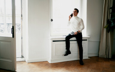 talking on the phone and standing near the window. the work done on the new startup. A designer in a comfortable modern suit looks at the computer. Portrait of an adult creative person.