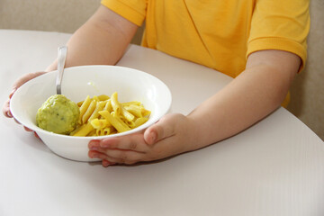 the child eats pasta and cutlet for breakfast or lunch in a white plate on a white table