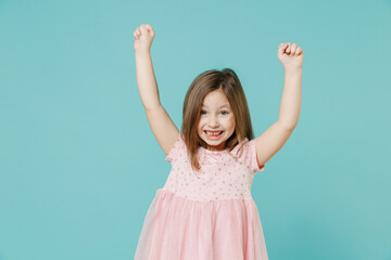 Little fun cute kid girl 5-6 years old wears pink dress doing winner gesture say yes isolated on pastel blue color background child studio portrait. Mother's Day love family people lifestyle concept.