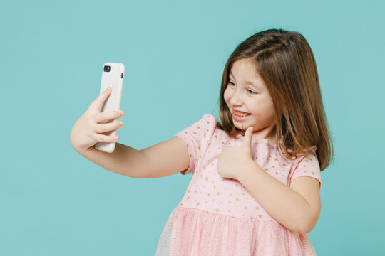 Little fun kid girl 5-6 years old wear pink dress doing selfie shot on mobile phone post photo on social network isolated on pastel blue color background child studio Mother's Day love family concept
