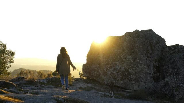 Caucasian young woman with brown dog seeing Sortelha nature mountain landscape with sun flare on a boulder, in Portugal