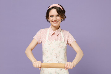 Young smiling happy confident housewife housekeeper chef cook baker woman in pink apron using rolling pin look camera isolated on pastel violet background studio portrait Cooking food process concept