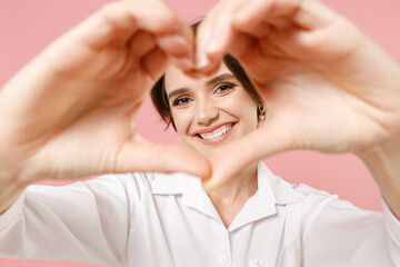 Young employee business woman corporate lawyer in classic formal white shirt work in office showing shape heart with hands look through close up heart-shape sign isolated on pastel pink background