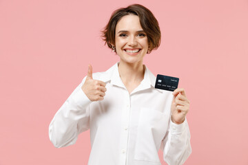 Happy young employee business secretary woman 20s corporate lawyer in classic formal white shirt work in office hold credit bank card show thumb up gesture isolated on pastel pink background studio.