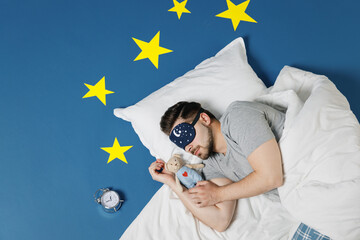 Top view young man in pajamas jam sleep mask resting relax at home lies wrap covered under blanket...