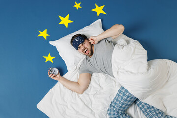 Top view young man wear pajamas jam sleep mask rest at home lies wrap covered under blanket cover...