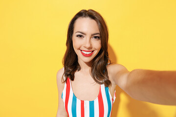 Fototapeta premium Close up happy fun young sexy woman slim body wear striped red blue one-piece swimsuit doing selfie shot isolated on vivid yellow color background studio. Summer hotel pool sea rest sun tan concept.