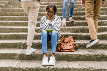 Upset victim of abuse or racism sitting on stairs outdoors with backbag.