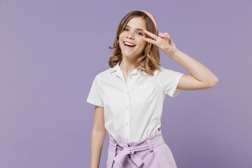 Little friendly smiling happy blonde kid girl 12-13 years old in white shirt cover eye with victory v-sign gesture isolated on purple background children studio portrait. Childhood lifestyle concept.