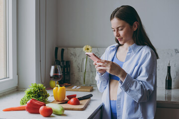 Young vegan fun housewife woman 20s in casual clothes blue shirt prepare salad using mobile cell...