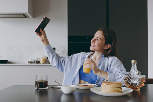 Young housewife woman in casual clothes blue shirt eat breakfast pancakes do selfie shot mobile phone post photo social network cook food in light kitchen at home alone Healthy diet lifestyle concept.