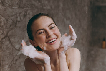 Close up smiling half naked topless young wet haired woman 20s taking shower wash face with...