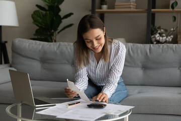 Happy young woman holding paper bills in hands, calculating expenditures, paying bills or services...