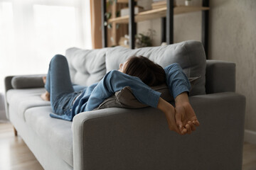 Rear full length view relaxed millennial woman lying on comfortable sofa, daydreaming napping or meditating alone, enjoying peaceful carefree weekend time at home, breathing fresh air indoors.