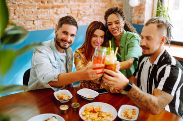 Group of young friends meeting in a cafe. Two women and two men in a cafe talking, laughing, drinking cocktails and eating.  People, lifestyle, lunch, party, relax concept.