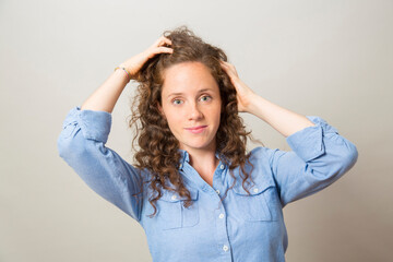 Fototapeta premium portrait pretty redhead smiling girl with hand in hair wearing blue shirt looking at camera with on gray background