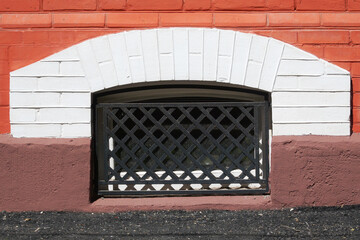 A window with a lattice to the basement of an old brick house.