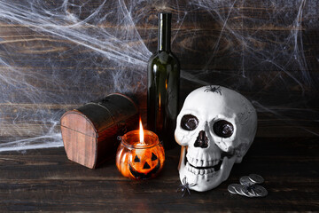 Human skull, dark glass bottle, coins, casket and burning candle in glass candlestick in the form...