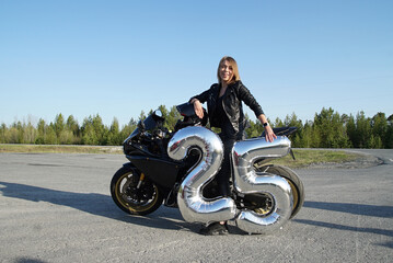 A girl with fair hair and a leather jacket on a black motorcycle.She enjoys the summer sun and life.