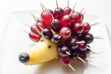 Fruit hedgehog, red grapes and juicy pear, creative way of serving fruit - obrazy, fototapety, plakaty