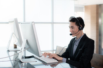 Smiling businessman wearing microphone headsets is working as customer care operator or help desk service and team support information in call center office.