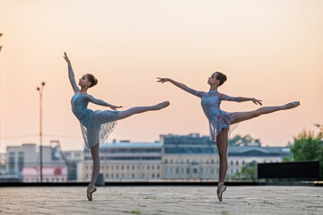 Fototapeta na wymiar Two young ballerinas dancing in pointe shoes in city against the backdrop of sunset sky