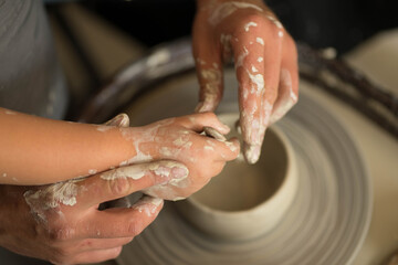 human hands make a clay product on a potter's wheel