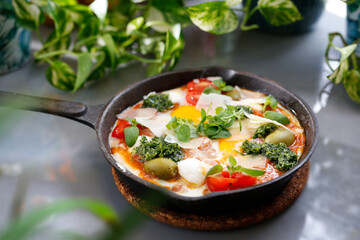 Shakshouka, fried eggs in a pan with vegetables and tomatoes.
Breakfast, eggs with vegetables served in a pan.