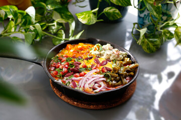 Shakshouka, fried eggs in a pan with vegetables and tomatoes.
Breakfast, eggs with vegetables served in a pan.