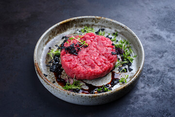Modern style gourmet tartar raw from beef filet with herbs and spices served as close-up on a Nordic design plate with copy space