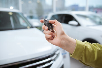 Close up cropped shot of a car key in female driver hand, cars at dealership on background