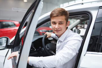 Young man smiling to the camera, getting out of the car at dealership salon