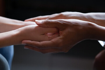 Close up young african american woman holding hand of female caucasian friend, giving psychological help, supporting in difficult life situation. Sincere mixed race people holding trusted conversation