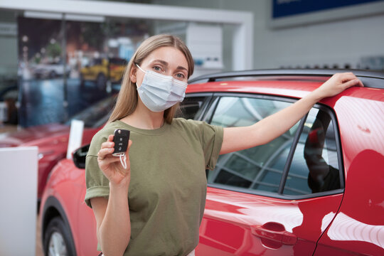 Woman wearing medical face mask while buying new auto at car dealership, showing car key
