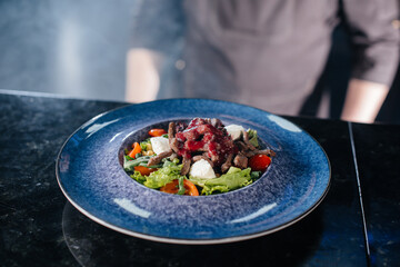 A professional chef serves a freshly prepared salad of tomato and veal greens with sauce in a gourmet restaurant close-up.