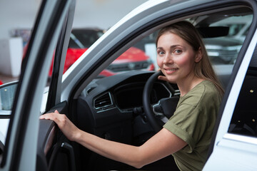 Plakat Cheerful female driver sitting in a new auto at car dealership