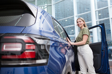 Woman examining automobile for sale at car dealership, copy space