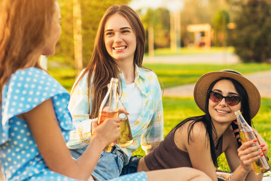 The image of the best friends, young beautiful women together on a picnic, chatting and having fun while sitting on the grass