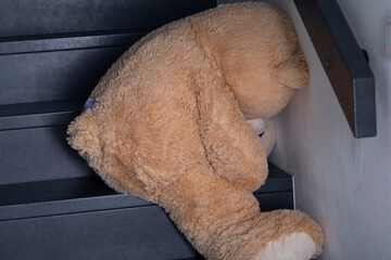 Teddybär sitzt beleidigt auf der grauen Treppe, auf der Stufe. sein Kopf ist genickt an der Wand. Sehr wahrscheinlich ein Kind hat ihn abgelegt und will mit ihm nicht spielen. Bär bestraft