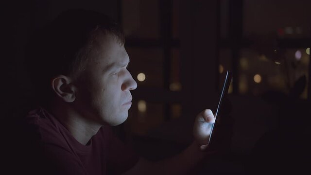 Close-up man face, light from mobile phone screen, man browsing mobile applications, night shooting