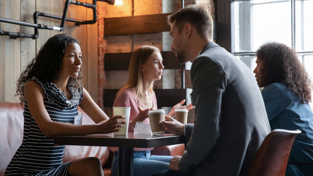 Happy young diverse people enjoying speed dating communication, discussing common interests in cozy cafeteria. Shy millennial generation mixed race men and women chatting talking at meeting.