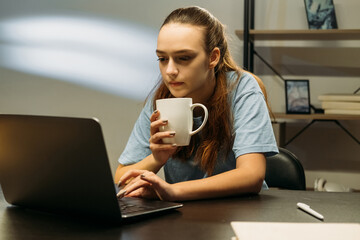 Work from home. Coffee break. Lockdown business. Relaxed woman working on laptop typing in office workspace drinking from cup