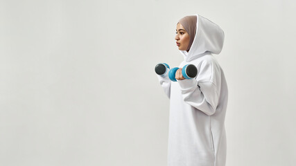 Cute young arabian woman in hijab holding dumbbells