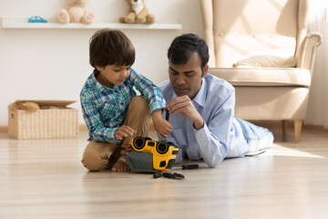 Caring young Indian father teach small cute curious ethnic son repair toy car at home. Loving mixed...