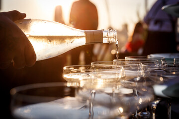  Sunset closeup view of a Waiter's hand pouring sparkling wine into glasses at a party.